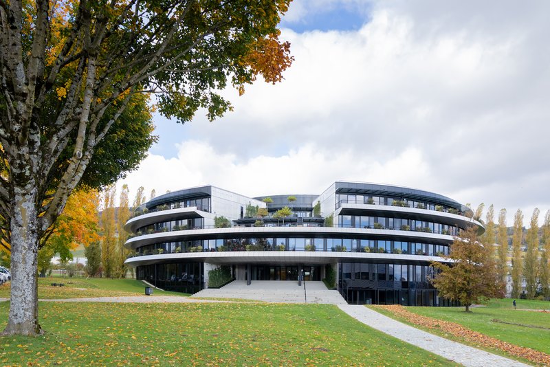 Curved facade with continuous balconies rising above a green lawn with autumn trees
