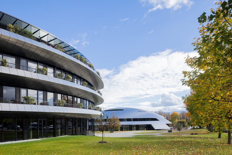 Planted rooftop terrace above curving balconies facing a white disc building across the lawn