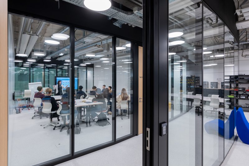 Glass-walled conference room with meeting in progress under exposed ceiling and pendant lights