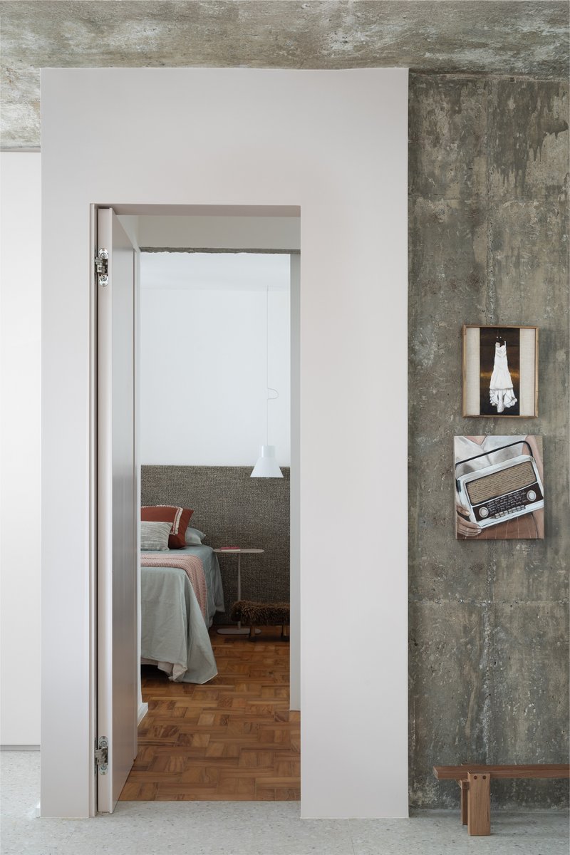 Open doorway revealing bedroom with parquet flooring beyond the exposed concrete and white plaster walls
