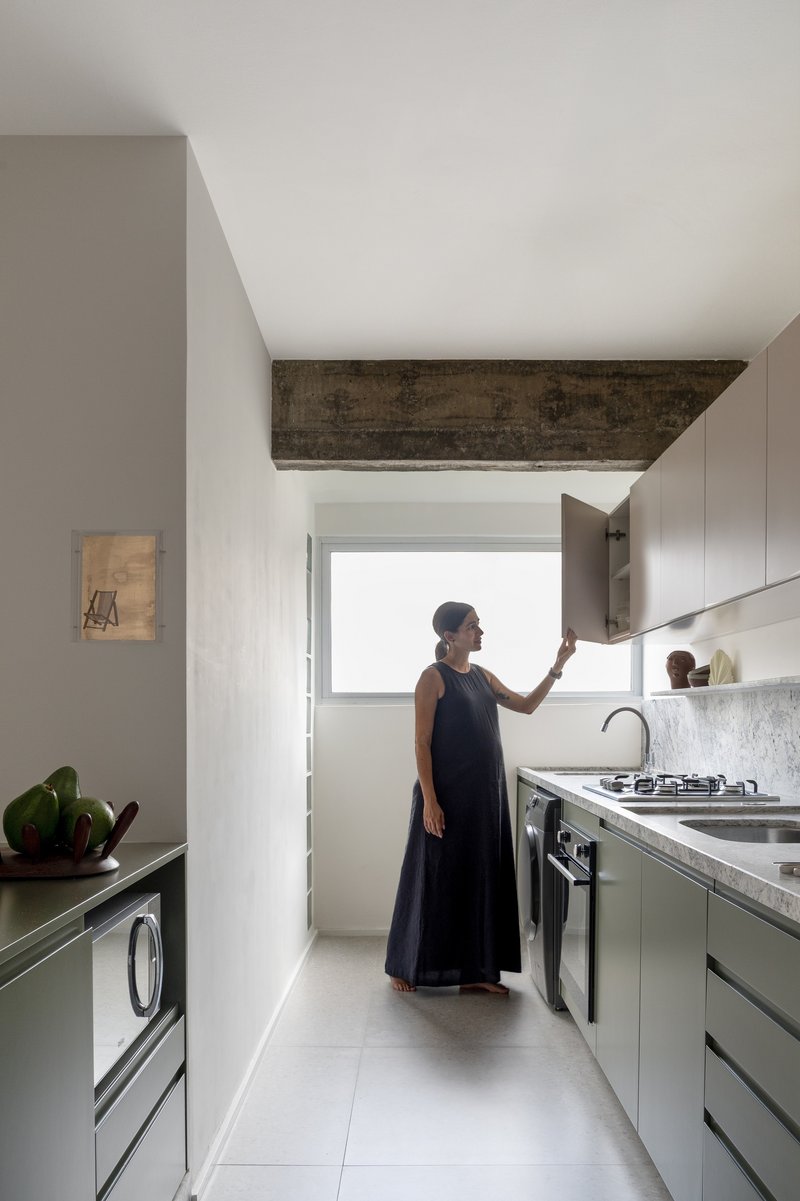 Galley kitchen with exposed concrete beam overhead and a woman opening an upper cabinet