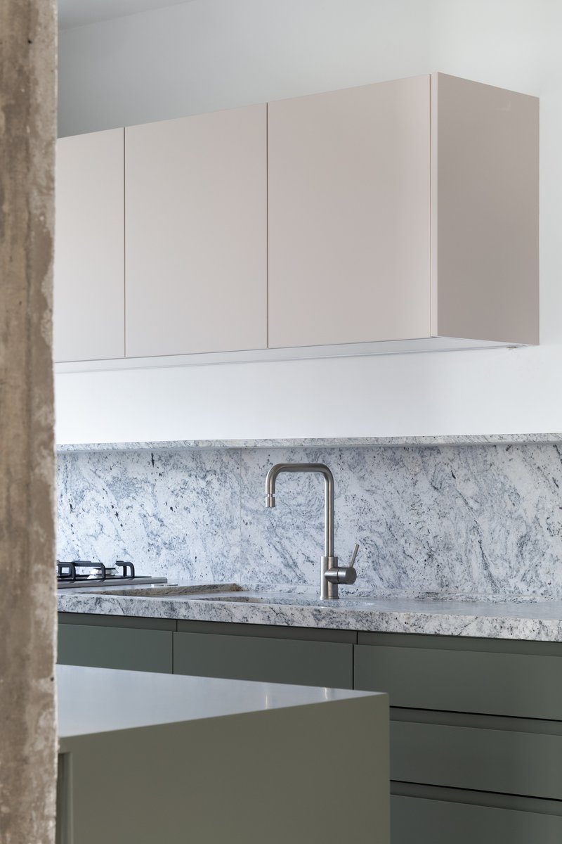 Kitchen counter detail showing white marble backsplash with sage green lower cabinets and steel faucet
