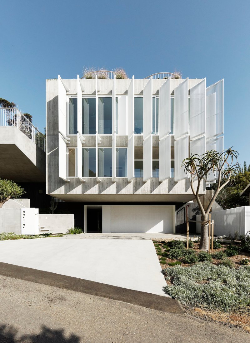 Street facade showing white vertical louvres wrapping the upper floors above a recessed garage entry