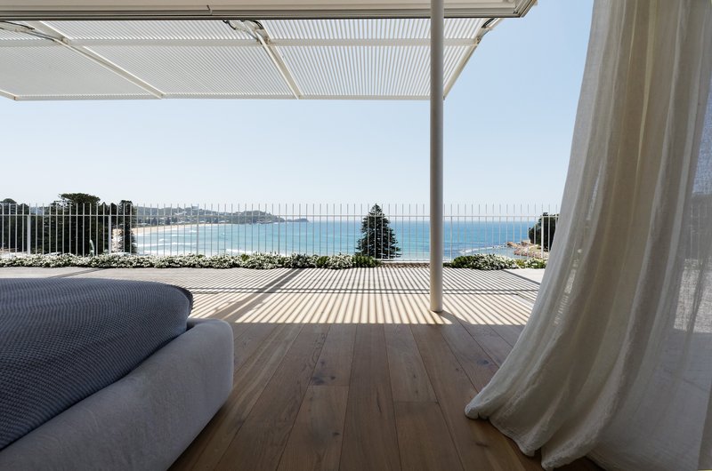 Covered terrace with timber decking and slatted canopy overlooking the ocean beyond a steel balustrade