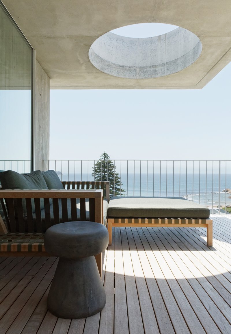 Outdoor terrace with timber furniture and circular skylight cut into the concrete soffit above