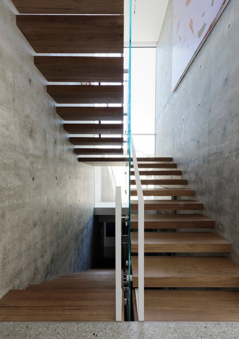 Timber staircase with open treads ascending between board-formed concrete walls and glass balustrade