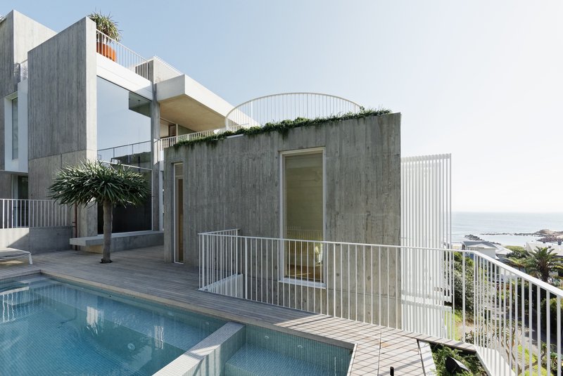 Pool deck with curved concrete pavilion and white metal railings overlooking the coastline
