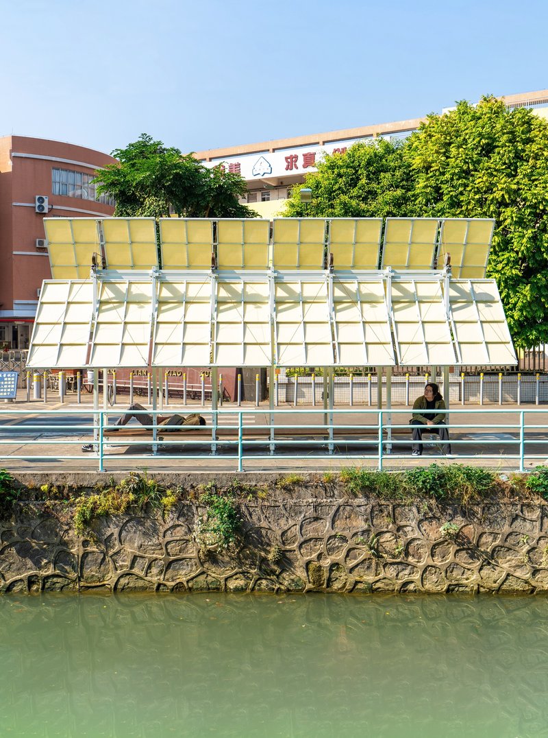 Sloped canopy with translucent yellow panels and steel frame above a stone embankment wall