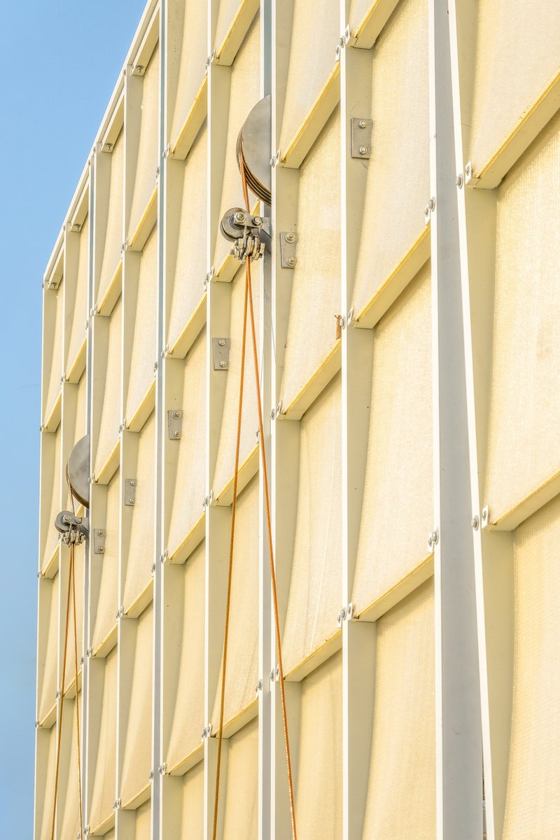 Close-up of the vertical yellow fabric panels with metal clips and cables against blue sky