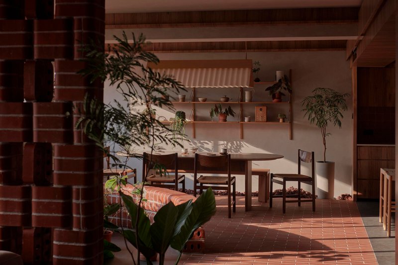 Dining area with brick tile floor and freestanding plants in afternoon sunlight filtering through screens