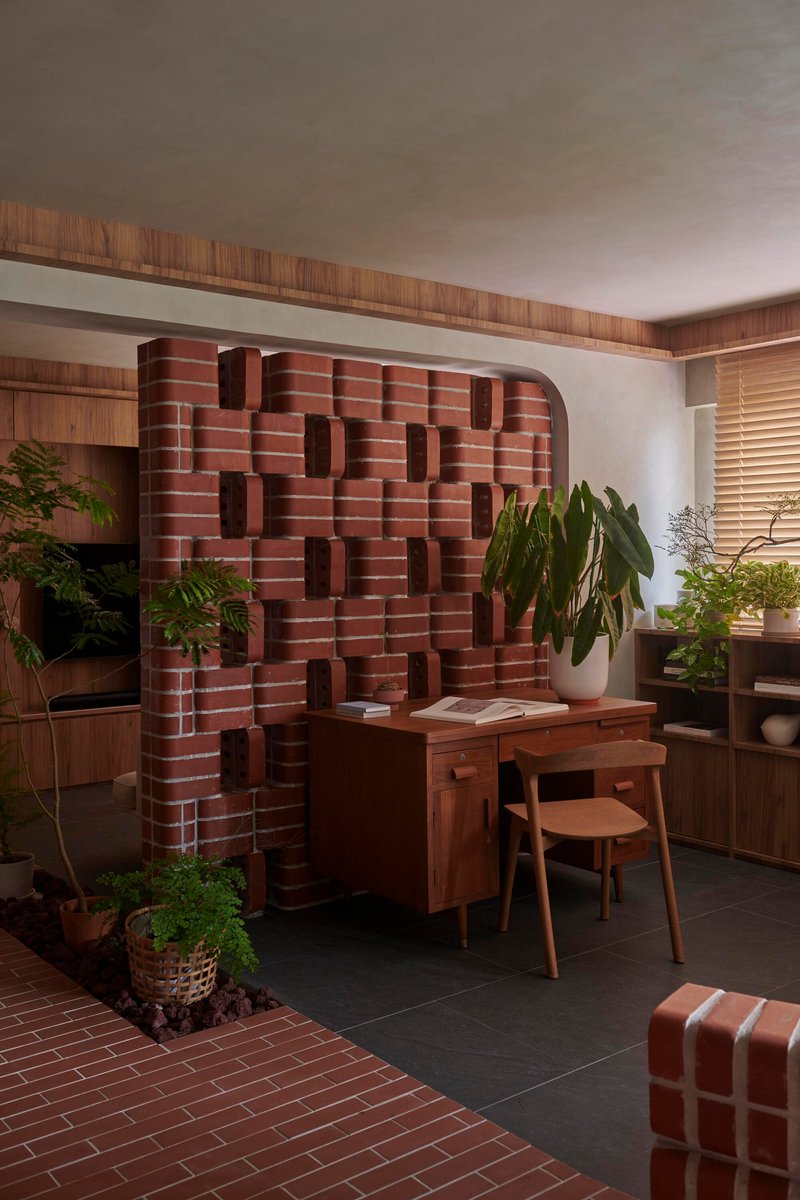 Sculptural red brick wall with protruding blocks behind a timber desk and potted plants