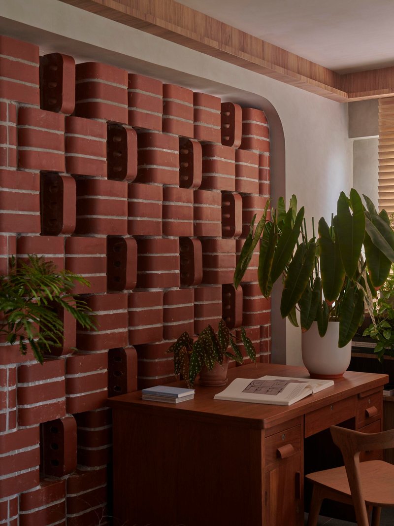 Close-up of the textured brick wall with recessed slots beside a desk with plants