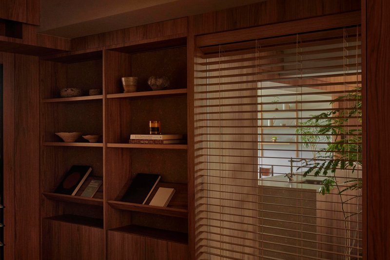 Timber bookshelf beside horizontal timber blinds screening a planted balcony beyond