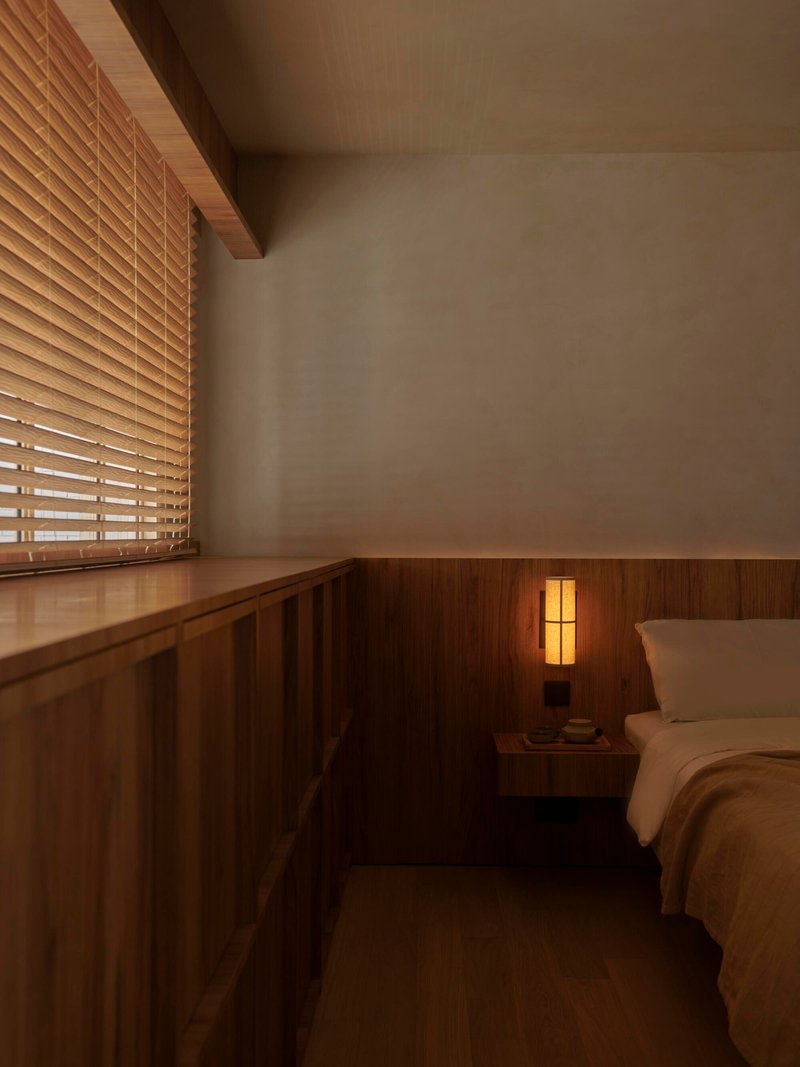 Bedroom corner with timber wall paneling, exposed timber beam and bedside table lamp in low light