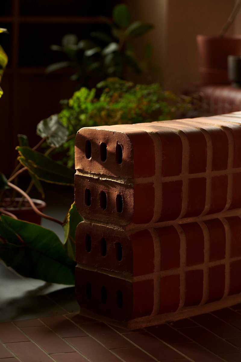 Close-up of terracotta brick stack with perforations beside potted greenery in dappled sunlight