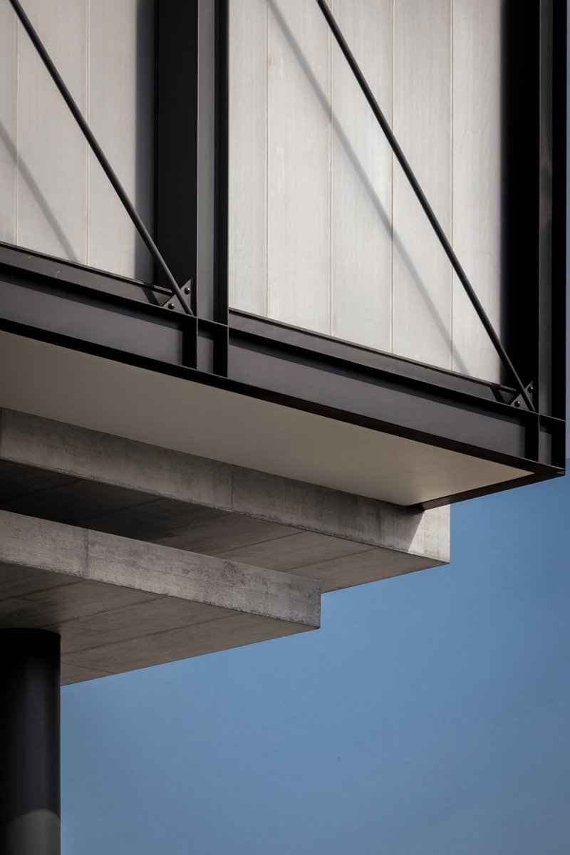Upward view of concrete cantilever slabs beneath a translucent facade with diagonal bracing against blue sky