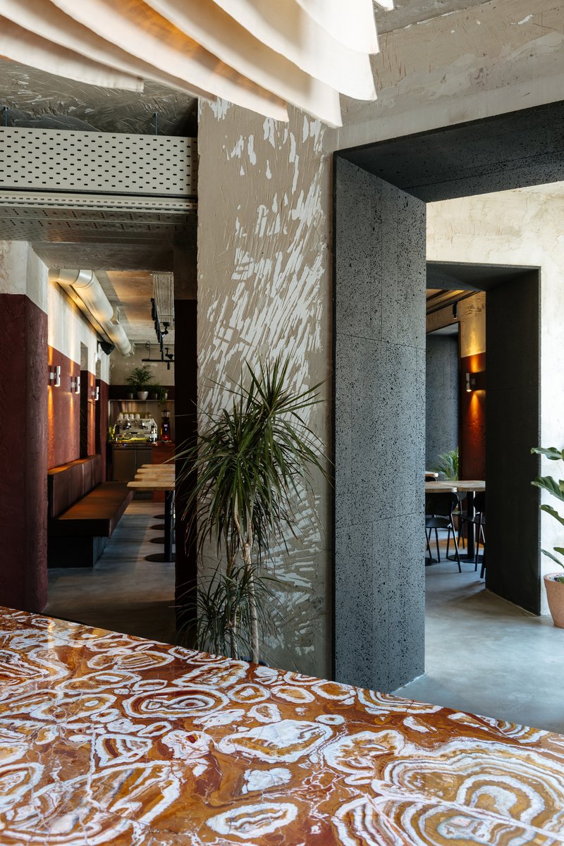 Concrete columns dividing rooms with polished terrazzo floor pattern and potted plants catching dappled light