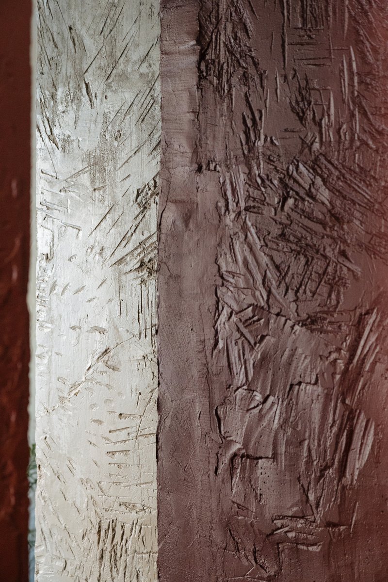 Close-up of textured plaster wall showing transition from white to terracotta with trowel marks
