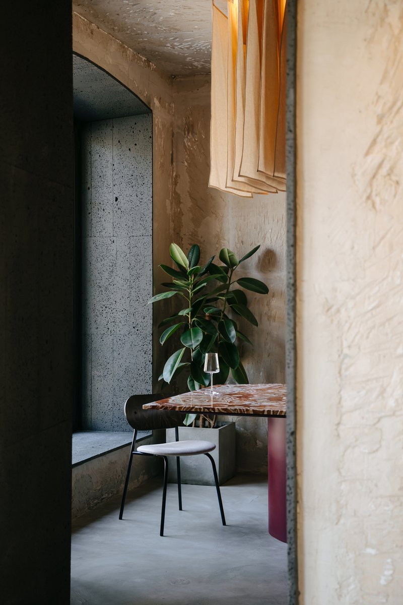 View through a doorway into a dining area with exposed concrete walls and a potted plant