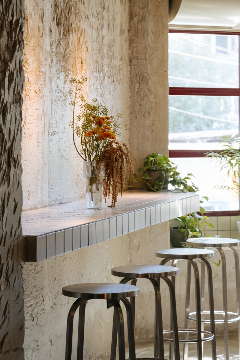 Bar counter with white tile face and metal stools against a textured plaster column