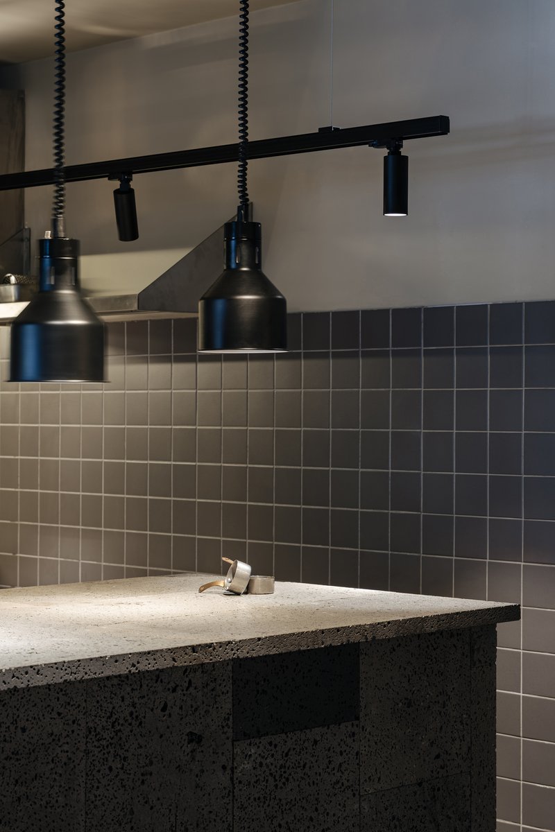 Bathroom sink with dark mosaic tile backsplash and black pendant track lighting above