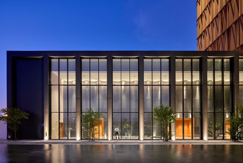 Glazed entrance facade with tall curtain wall and reflecting pool at dusk with a figure inside