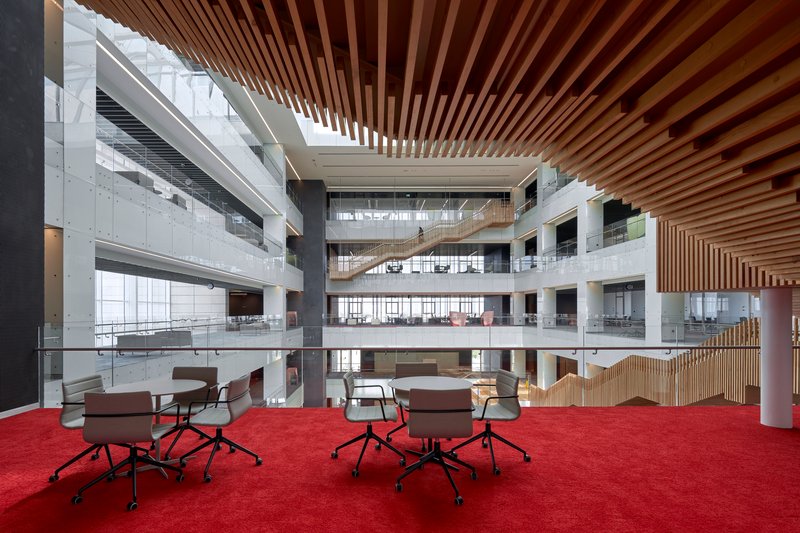 Atrium level with red carpeted floor and slatted timber ceiling above scattered work tables