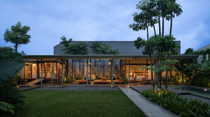 Garden facade of the glazed pavilion with flat roof and interior lighting at dusk