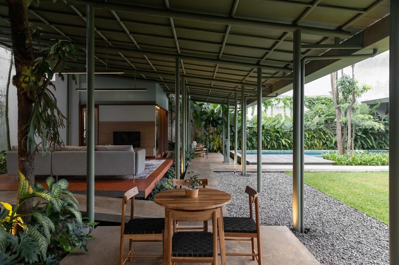Covered dining pavilion with slender steel columns and exposed gridded ceiling overlooking a gravel courtyard and pool