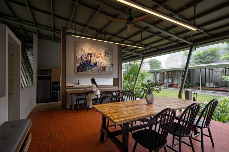 Open dining room with exposed steel structural grid and canted glazing framing a lawn and courtyard