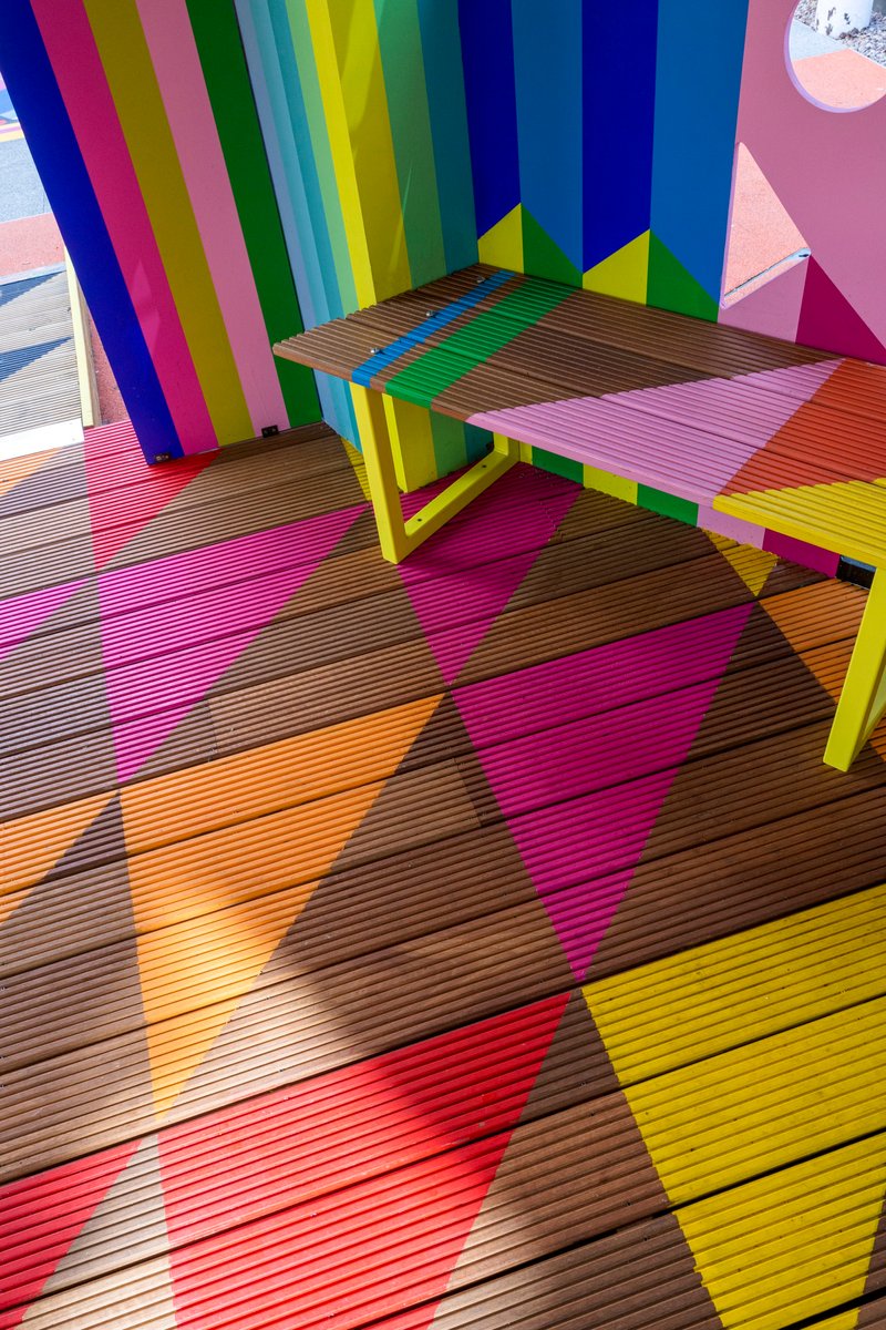 Overhead view of ribbed timber decking in diagonal multicolor bands and yellow painted bench legs