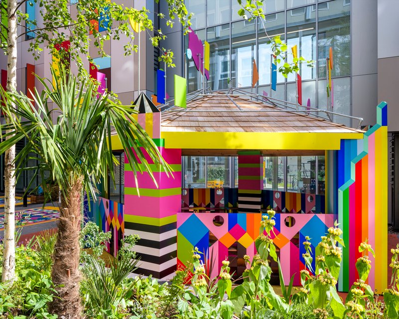Multicolored pavilion with striped columns and patterned facade surrounded by palm trees and planted beds