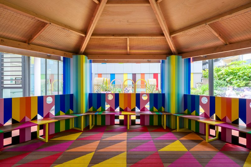 Interior view beneath timber ceiling showing wraparound bench seating with geometric wall panels and floor pattern