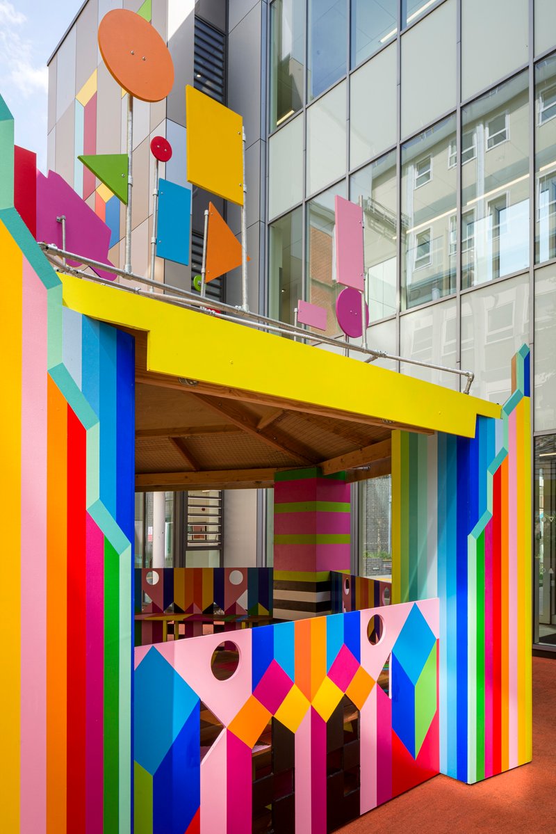 Close view of the pavilion entrance framed by vertical striped columns and geometric shapes on glass and balustrade