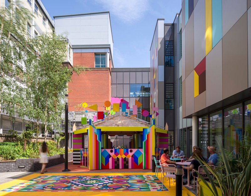 View across the courtyard showing the pavilion between residential blocks with pedestrians and seated groups on a sunny day