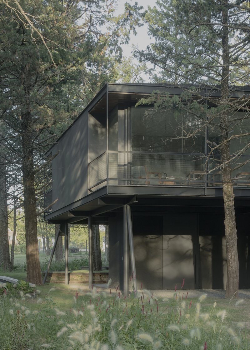 Cantilevered upper floor with wire mesh balcony and glass facade surrounded by native grasses