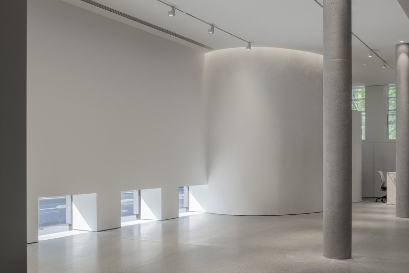 Curved white plaster volume beside concrete column with horizontal window slots at floor level