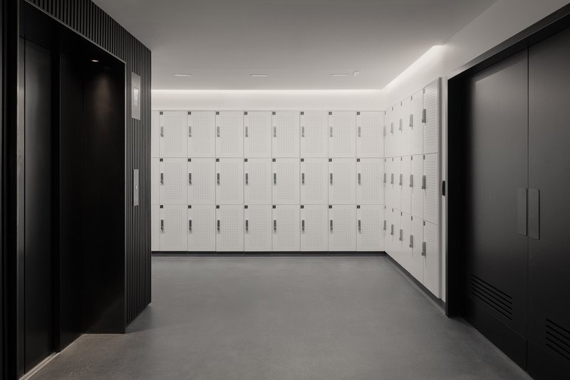 Locker room with white perforated metal lockers flanked by dark fluted wall panels and black storage units