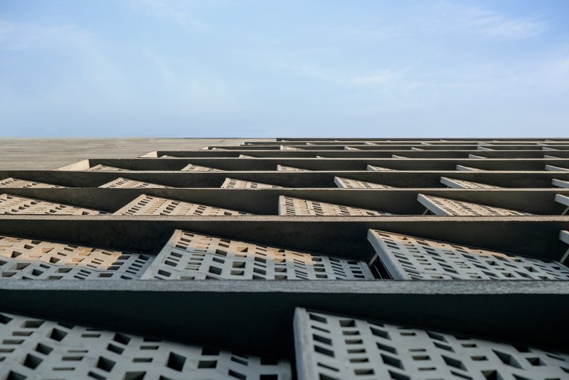 Looking up at the angled facade showing concrete diagonal bracing over perforated brick infill panels