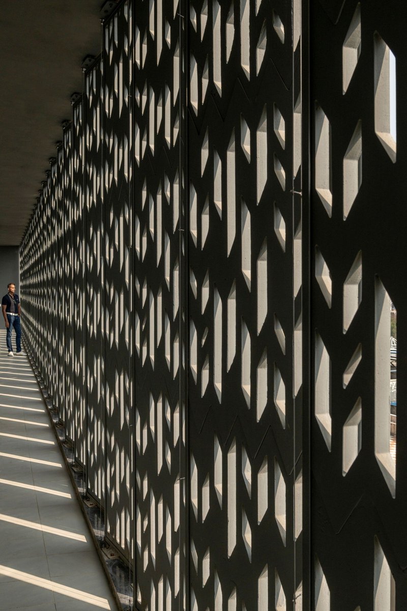 Chevron-patterned screen wall creating layered shadows along the interior walkway with a person standing