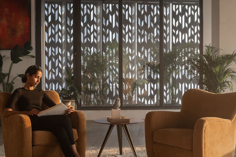 Interior seating area with decorative metal screen filtering daylight beside potted palms and upholstered chairs