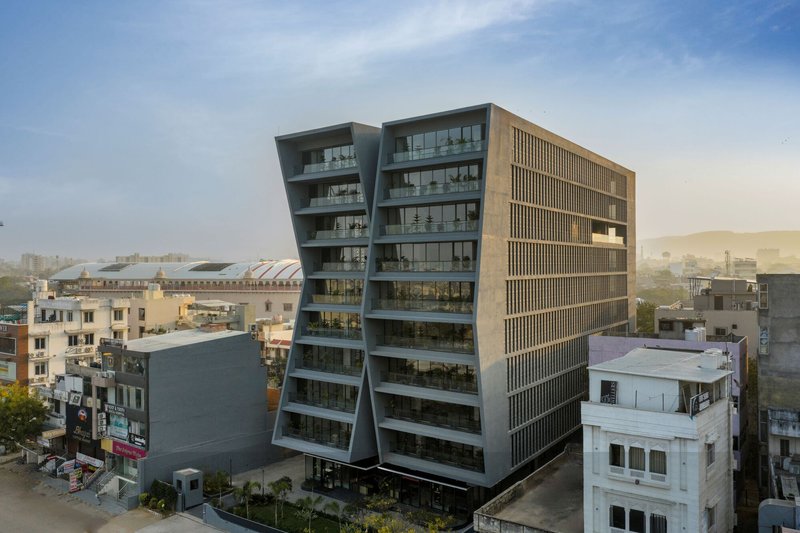 Aerial view of the angled glass and concrete tower rising above low-rise urban fabric in hazy afternoon light