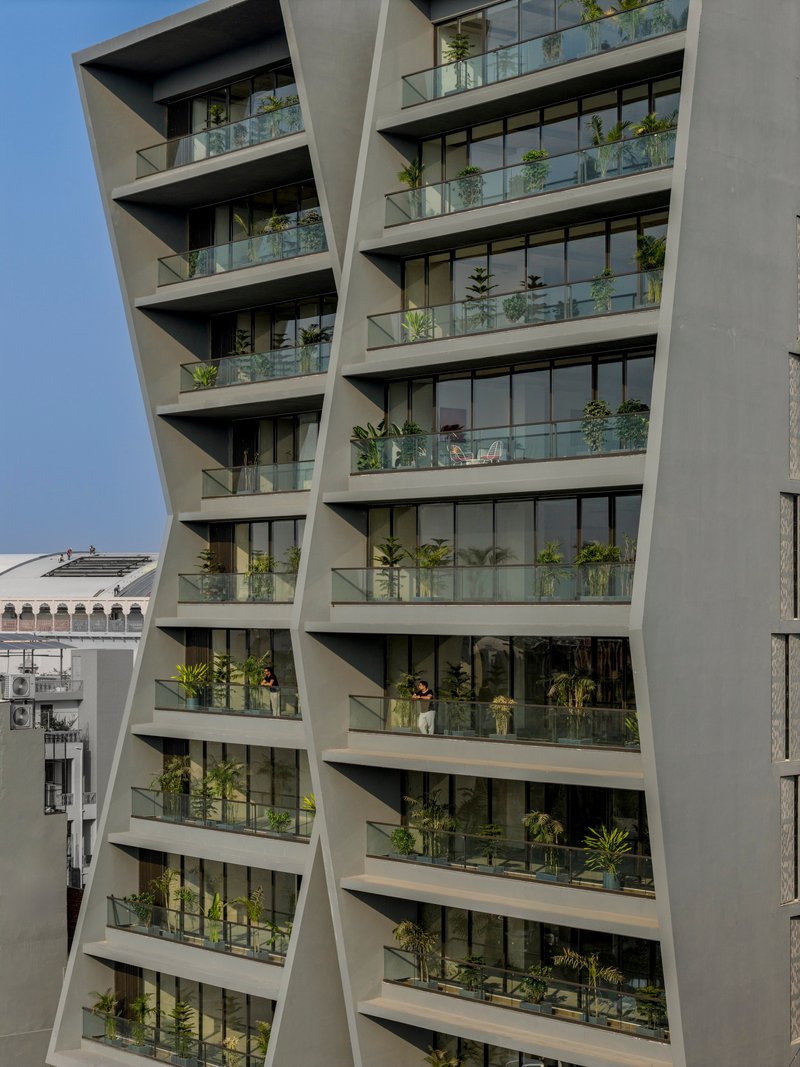 Diagonal facade with staggered balconies planted with greenery behind glass balustrades under clear sky
