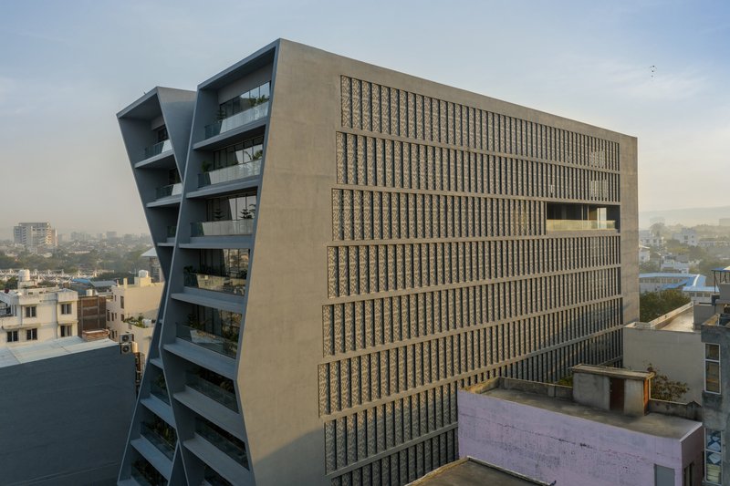 Side elevation showing the angled glass facade and perforated screen wall at dusk with distant hills