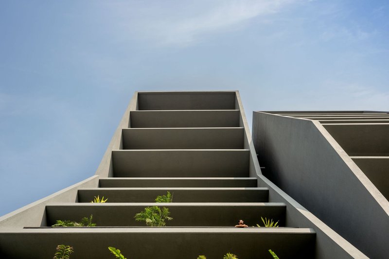 Upward view of stacked concrete balcony slabs with planted beds against blue sky
