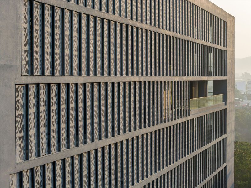 Facade detail showing alternating vertical concrete fins and patterned perforated brick panels between horizontal bands