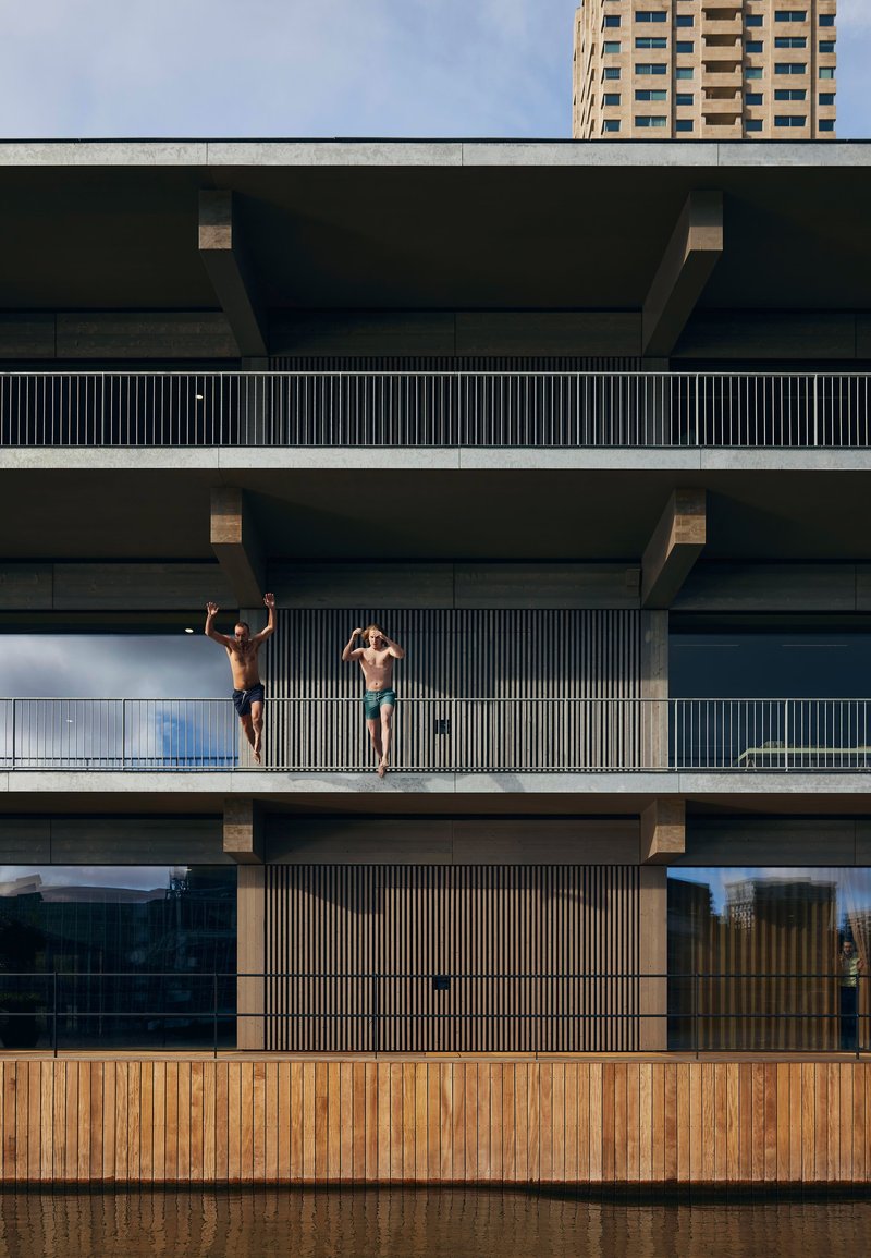 Stacked balconies with exposed concrete beams and vertical metal screens, two children mid-jump on upper level