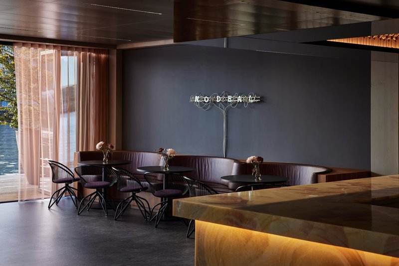 Lounge seating with curved banquette and onyx service counter near curtained waterfront windows