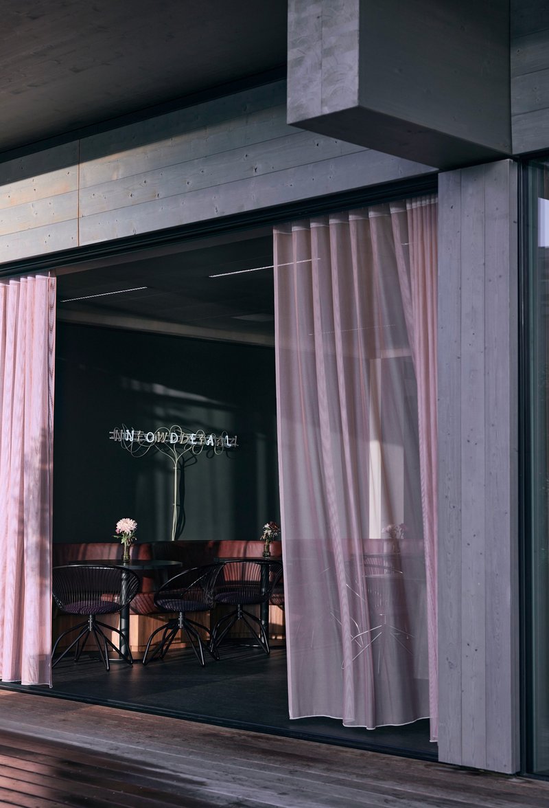 Exterior opening framed by concrete soffit and pink curtains with dining furniture visible inside at dusk
