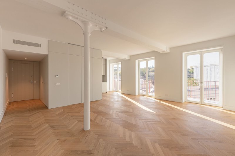 Open living space with herringbone oak flooring and a slender white column beneath sunlight